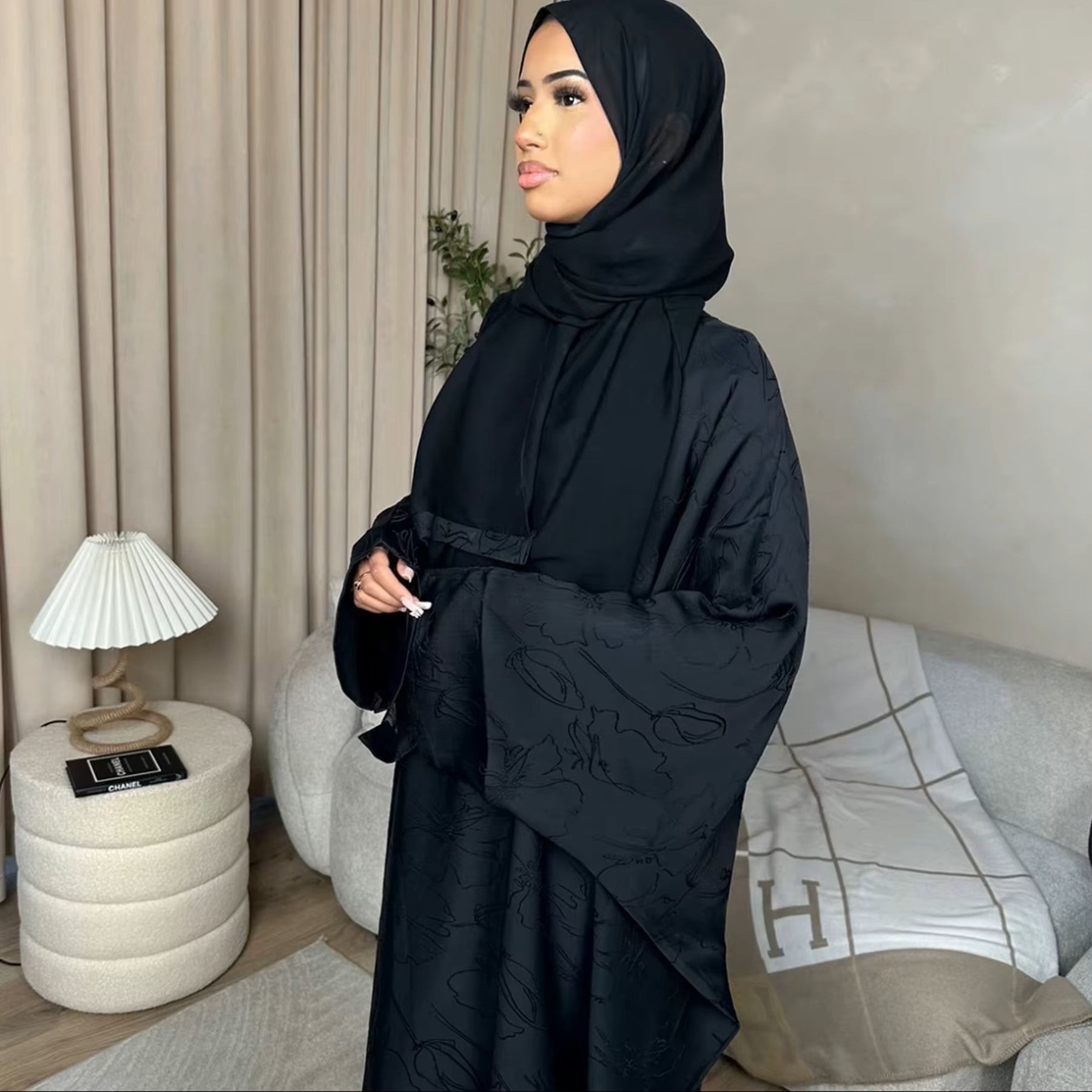 Woman in a dark green abaya and gray hijab sitting in a room with white walls and decorative elements - Canada hijab dress - USA MULSIMS