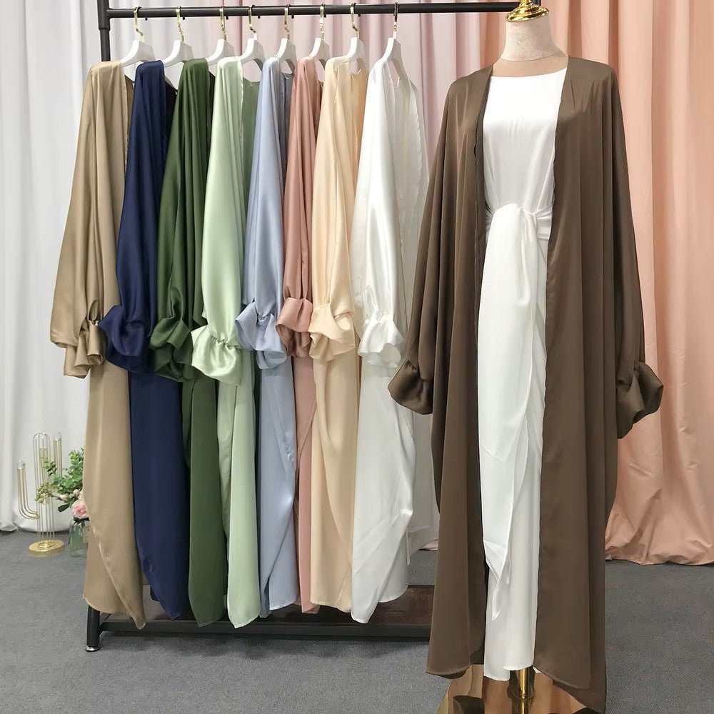 Colorful long cardigans on a rack with a mannequin wearing one against a pink curtain.