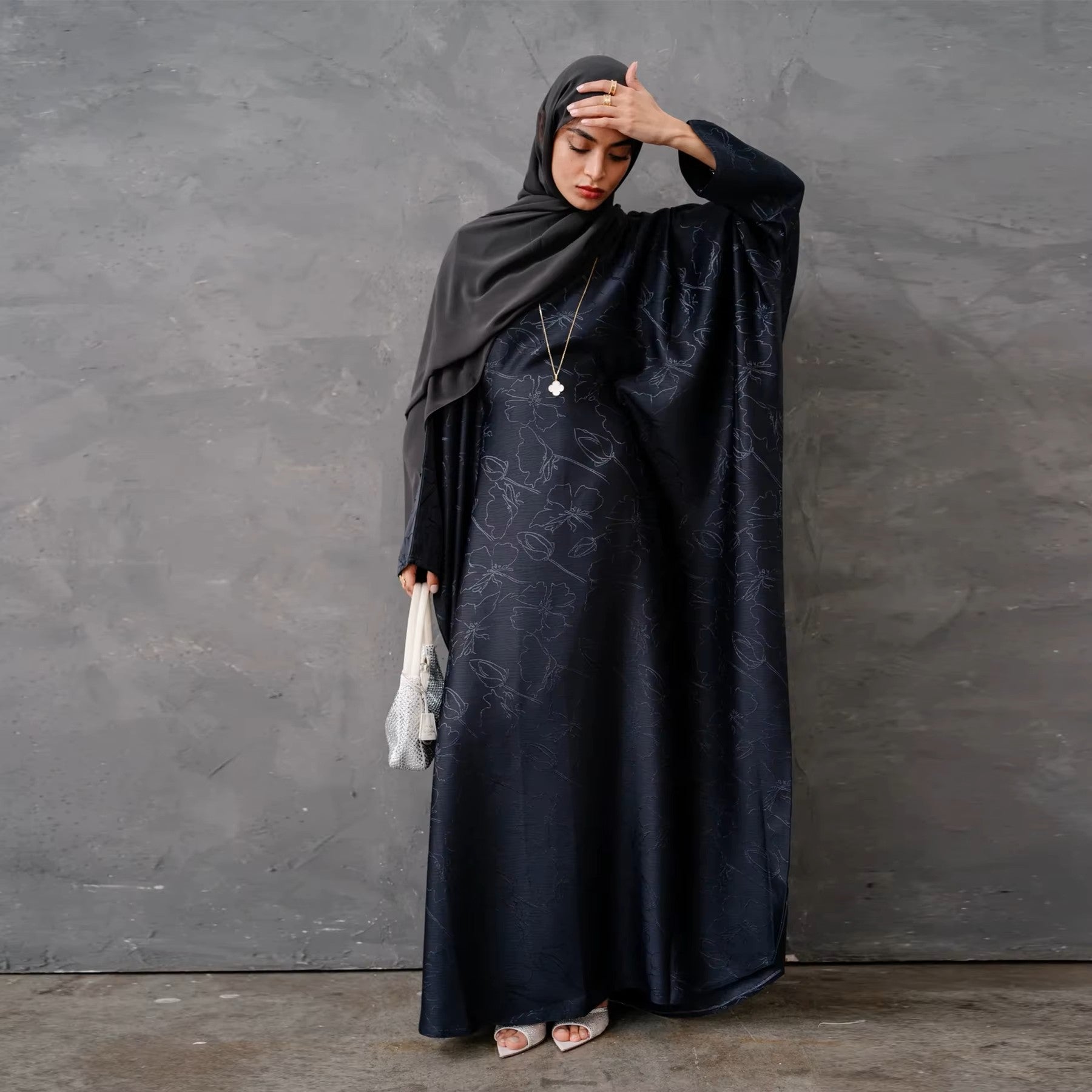 Woman in a dark green abaya and gray hijab sitting in a room with white walls and decorative elements - Canada hijab dress - USA MUSLIMS