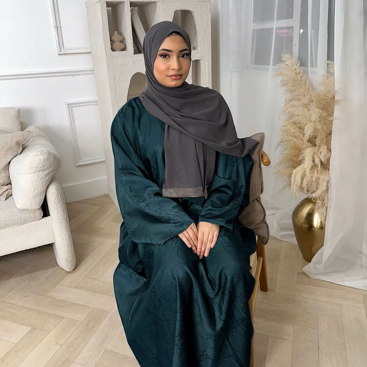 Woman in a dark green abaya and gray hijab sitting in a room with white walls and decorative elements - Canada hijab dress - USA MULSIMS