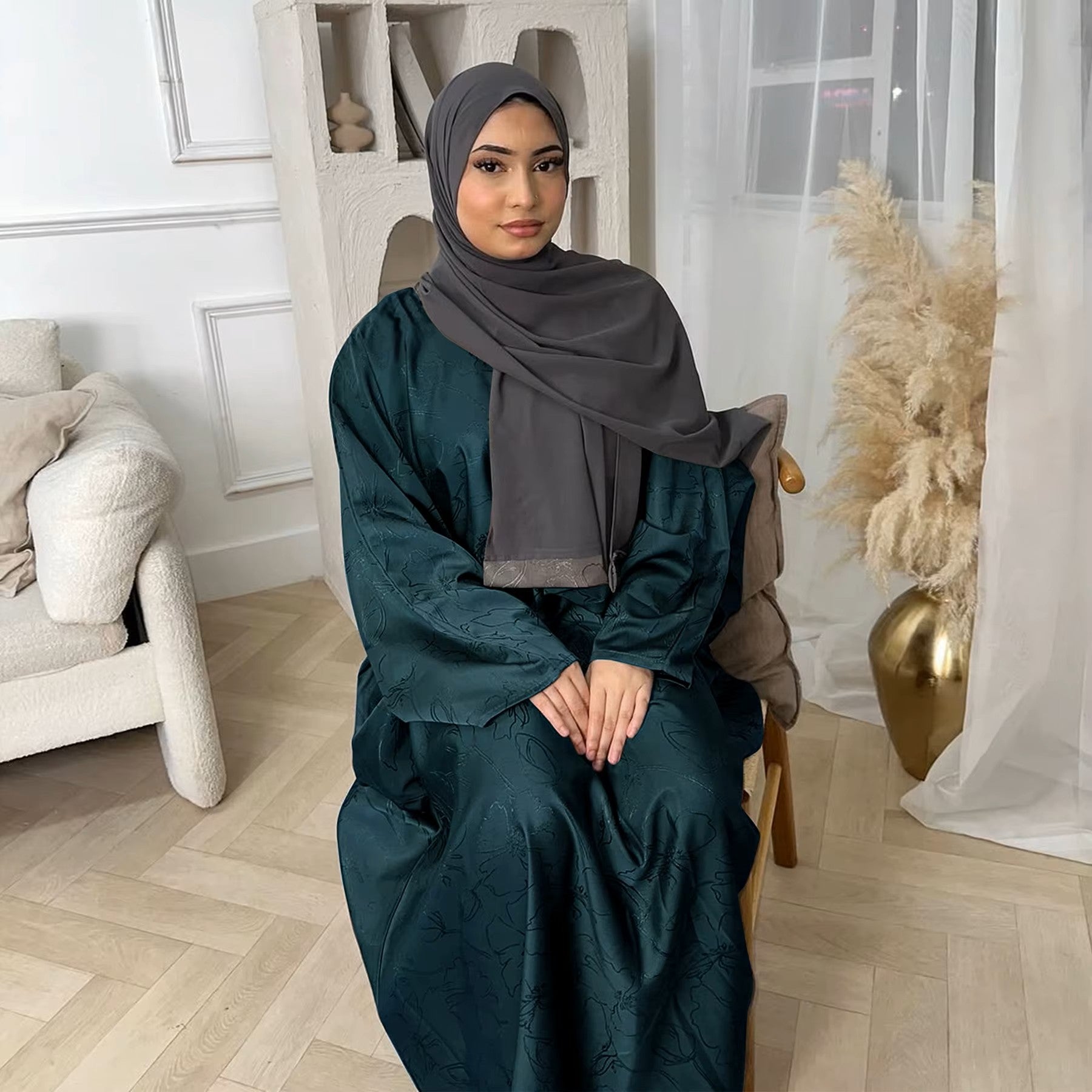 Woman in a dark green abaya and gray hijab sitting in a room with white walls and decorative elements - Canada hijab dress - USA MULSIMS