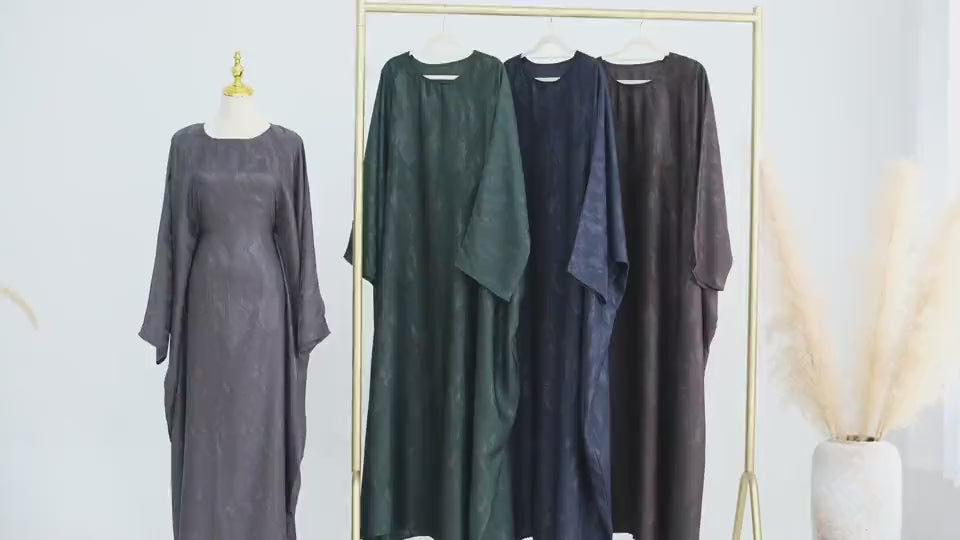 Woman in a dark green abaya and gray hijab sitting in a room with white walls and decorative elements - Canada hijab dress - USA MUSLIMS