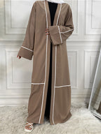 Brown abaya with white trim worn by a person against a white paneled wall.