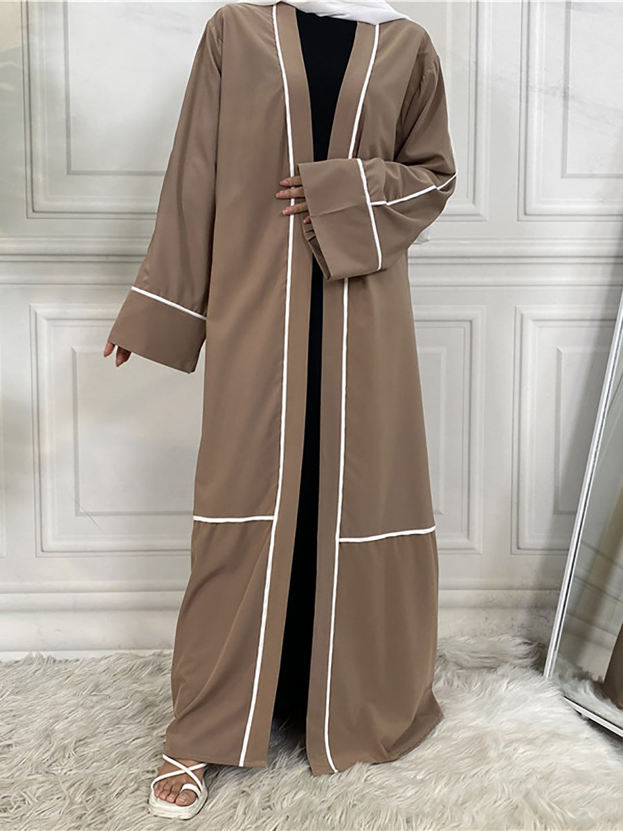 Brown abaya with white trim worn by a person against a white paneled wall.
