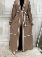 Brown robe with white trim on a person against a white paneled wall.