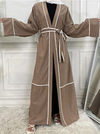 Brown robe with white trim on a person against a white paneled wall.