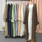 Colorful long cardigans on a rack with a mannequin wearing one against a pink curtain.