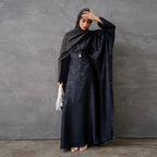 Woman in a dark green abaya and gray hijab sitting in a room with white walls and decorative elements - Canada hijab dress - USA MUSLIMS