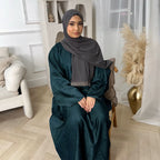 Woman in a dark green abaya and gray hijab sitting in a room with white walls and decorative elements - Canada hijab dress - USA MULSIMS